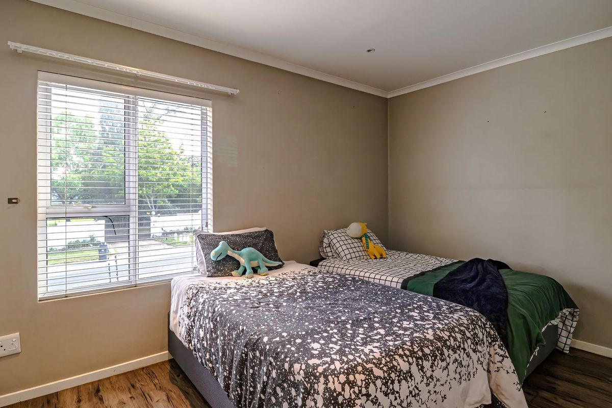 A bedroom featuring laminate flooring, neutral wall tones, and venetian blinds, providing a functional space with natural light.