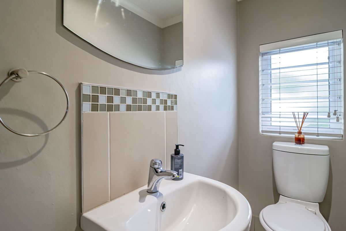 A clean and functional bathroom featuring a pedestal basin with chrome mixer tap, tiled splashback, wall-mounted mirror, and a standard toilet.