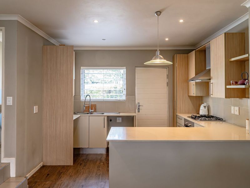 Modern kitchen featuring light wood cabinetry, stone countertops, gas hob, extractor fan, and a breakfast bar, with an adjacent view into a small bathroom.