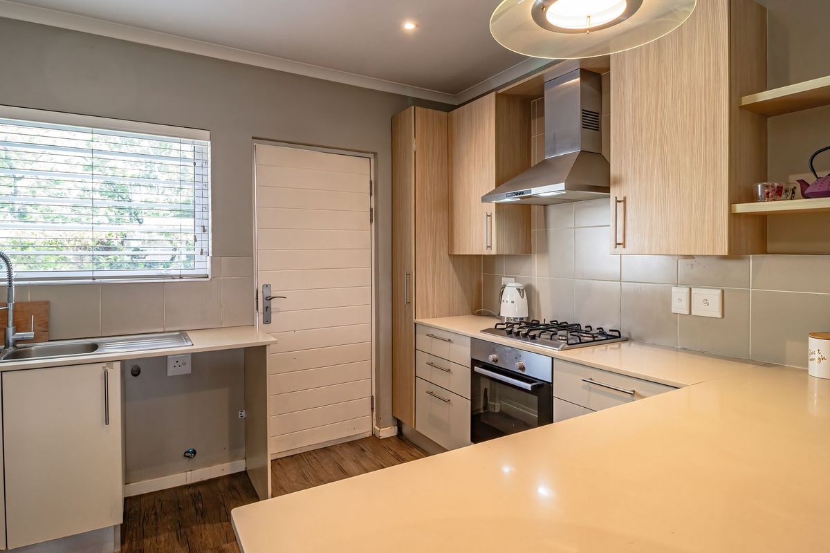 Modern kitchen featuring light wood cabinetry, stone countertops, gas hob, built-in oven, stainless steel extractor fan, and tiled splashback.