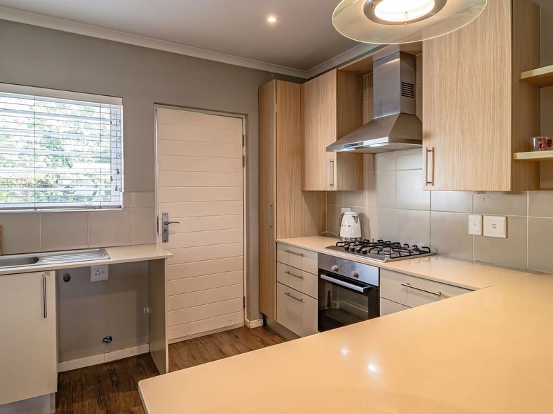 Modern kitchen featuring light wood cabinetry, stone countertops, gas hob, built-in oven, stainless steel extractor fan, and tiled splashback.