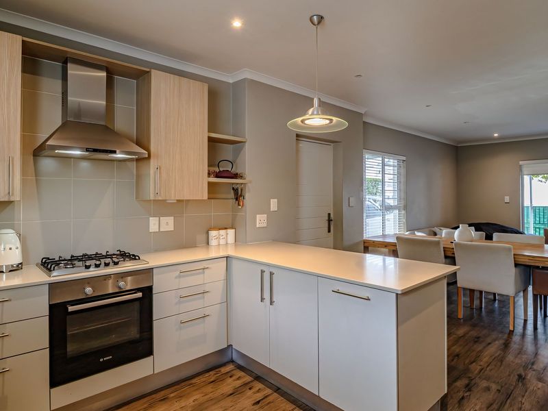 Modern open-plan kitchen featuring light wood and white cabinetry, stone countertops, and integrated appliances, flowing seamlessly into the dining and living area.