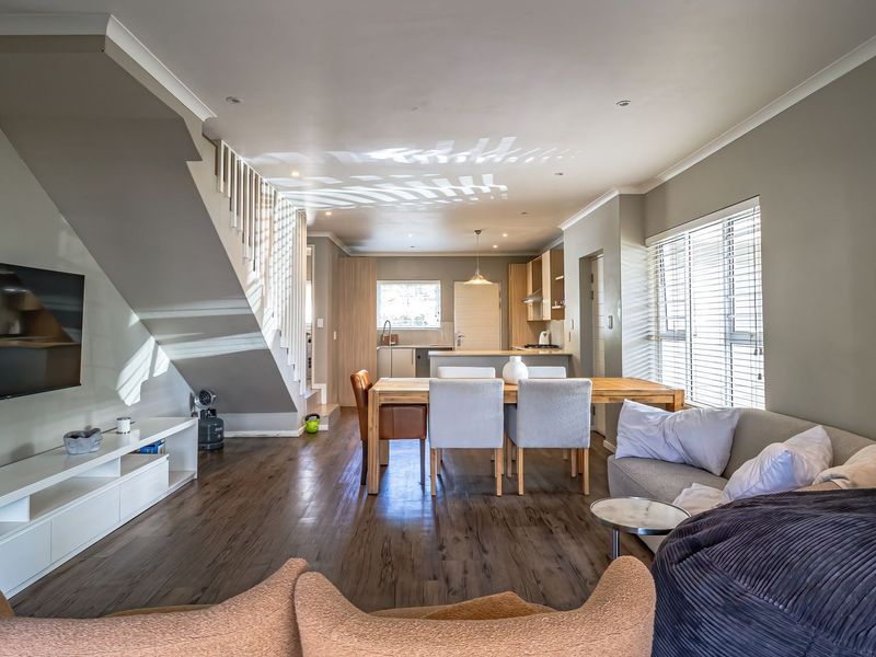 Spacious open-plan living and dining area featuring laminate flooring, a modern kitchen with island, and a staircase leading to the upper level.