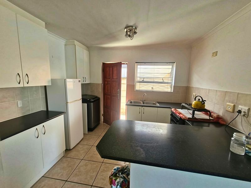 Functional kitchen featuring white cabinetry, dark laminate countertops, tiled flooring, and a double bowl sink with direct access to the exterior.