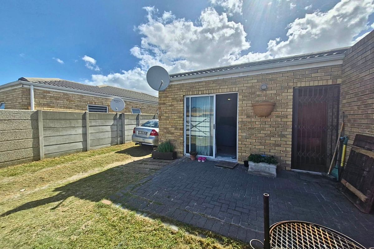 Rear exterior view of the property featuring a paved patio area, sliding door access, and a secure boundary wall.