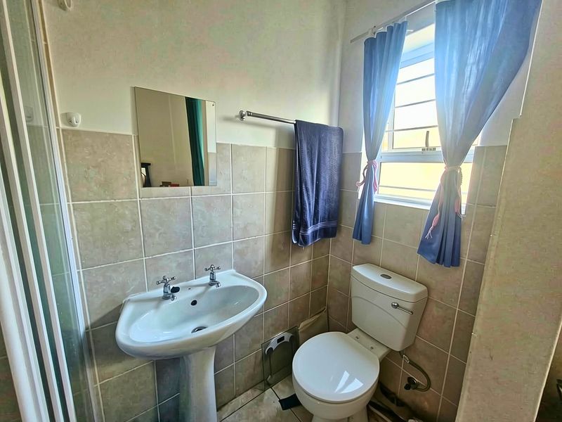 A functional bathroom featuring a pedestal basin, toilet, and shower enclosure with neutral wall tiling and a window for natural light.