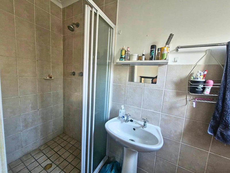 A functional bathroom featuring a pedestal basin, a tiled shower enclosure, and neutral wall tiling. The space would benefit from cosmetic updates.