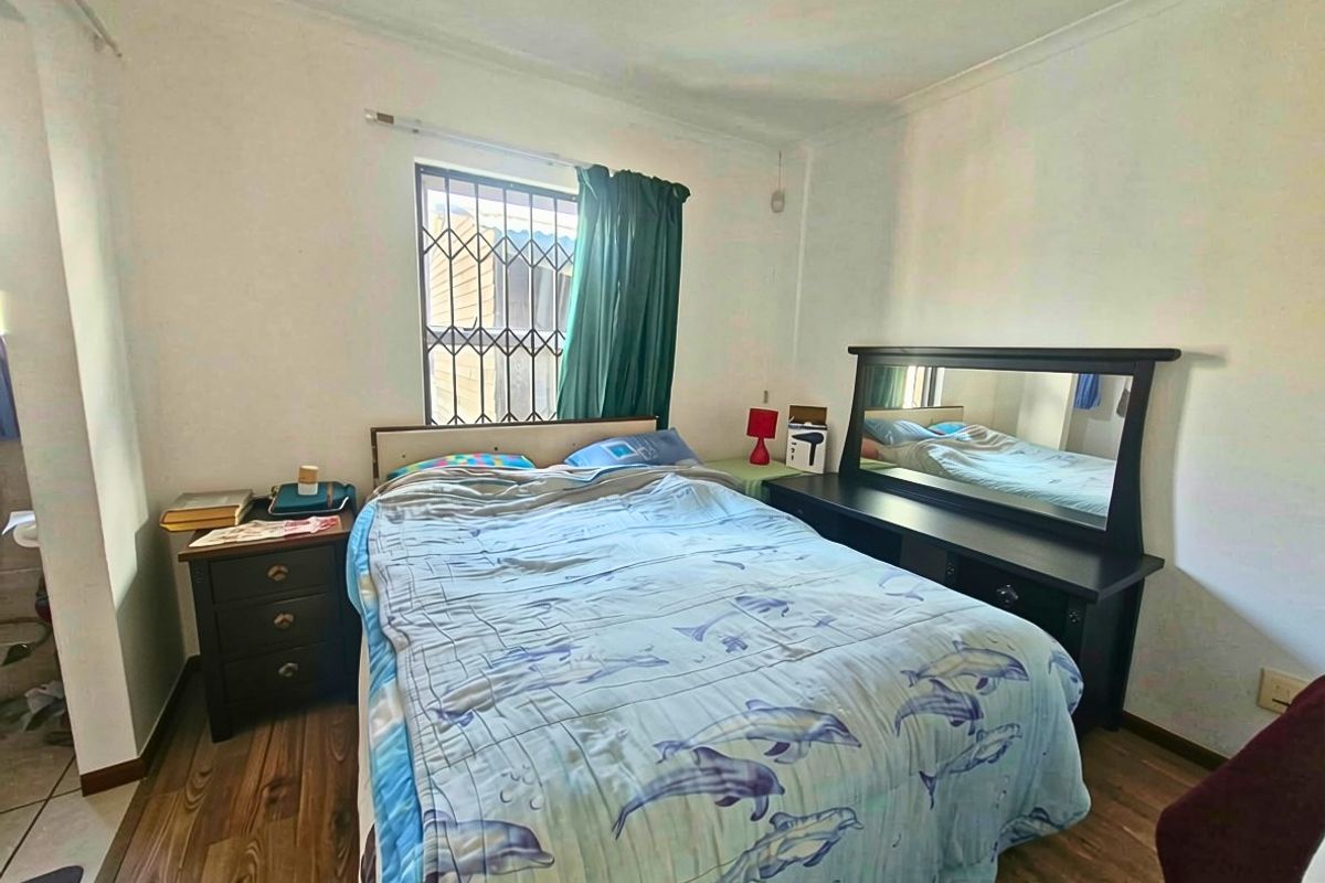 A standard bedroom featuring laminate flooring, coved ceilings, and a window fitted with security bars.