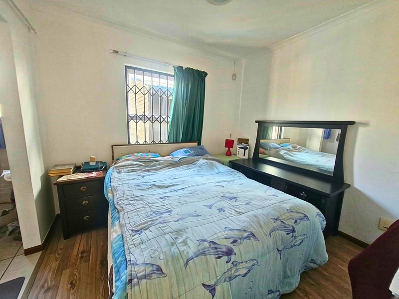 A standard bedroom featuring laminate flooring, coved ceilings, and a window fitted with security bars.