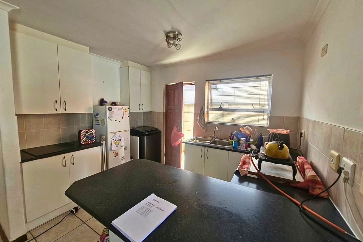 A functional kitchen featuring built-in cabinetry, granite countertops, a double sink, and tiled flooring with direct access to an exterior door.