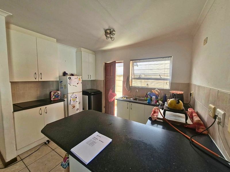 A functional kitchen featuring built-in cabinetry, granite countertops, a double sink, and tiled flooring with direct access to an exterior door.