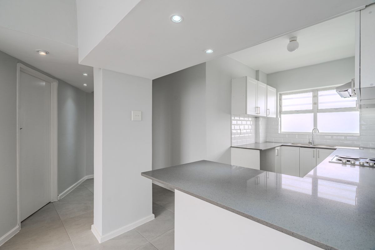 A modern, bright kitchen featuring clean white cabinetry, grey quartz countertops, subway tile backsplash, and integrated appliances in an open-plan layout.