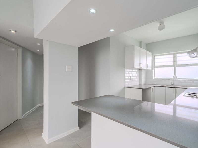 A modern, bright kitchen featuring clean white cabinetry, grey quartz countertops, subway tile backsplash, and integrated appliances in an open-plan layout.