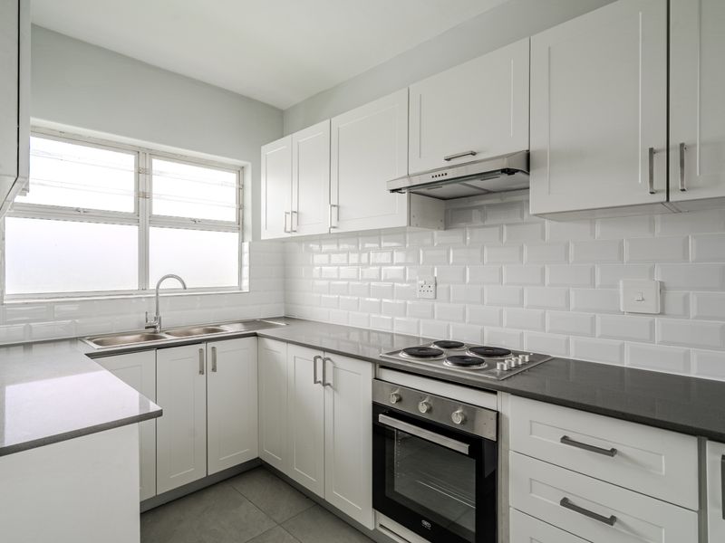 A modern, well-maintained kitchen featuring white shaker-style cabinetry, dark grey stone countertops, a subway tile backsplash, and integrated stainless steel appliances.