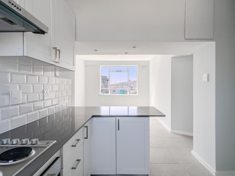 Modern kitchen featuring white cabinetry, dark stone countertops, subway tile backsplash, and integrated electric hob with extractor fan, leading to an open living area.