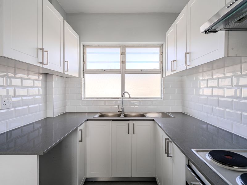 A clean, modern galley-style kitchen featuring white cabinetry, grey stone countertops, subway tile backsplash, and integrated stainless steel appliances.