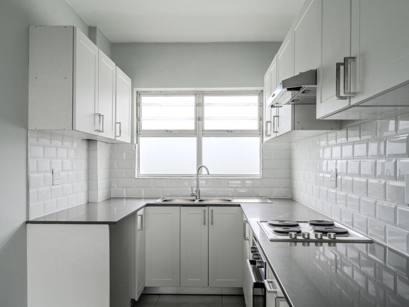 A clean, modern galley-style kitchen featuring white cabinetry, subway tile backsplash, grey stone countertops, and integrated stainless steel appliances.