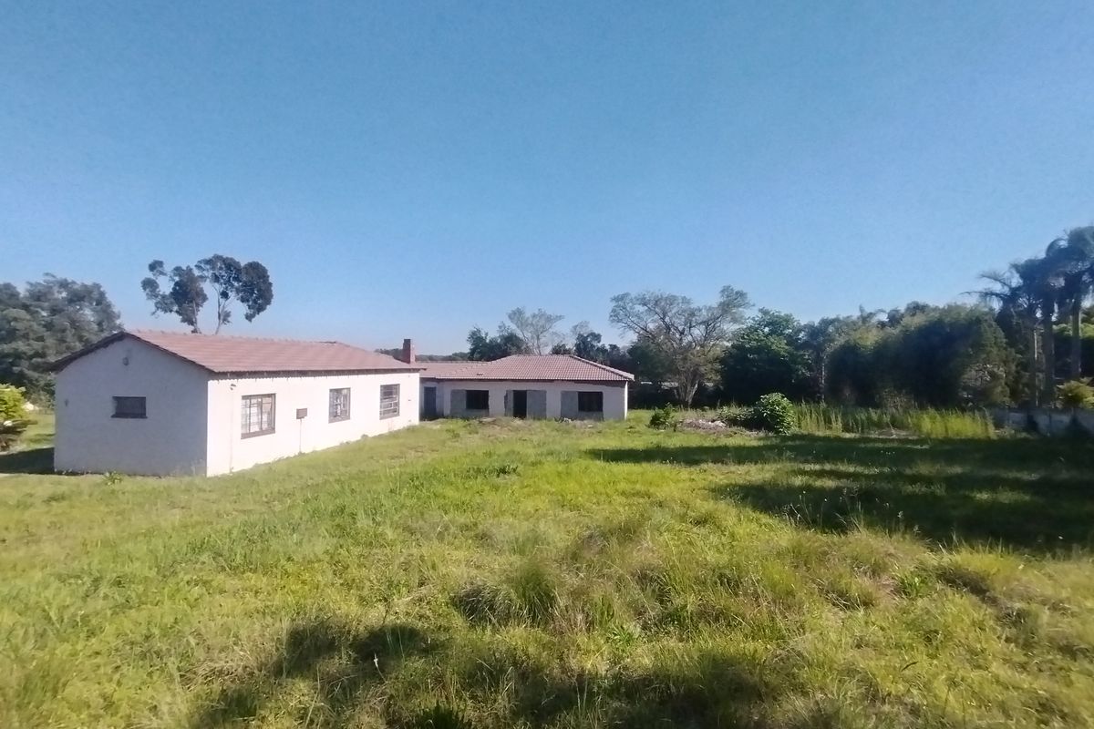 Rear view of a residential property featuring a tiled roof and masonry construction, set on a large plot with overgrown grass.