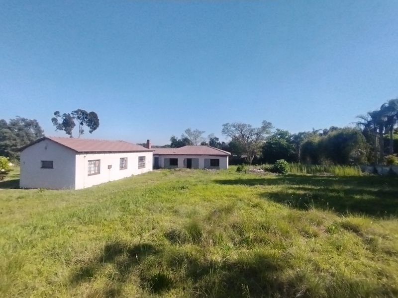 Rear view of a residential property featuring a tiled roof and masonry construction, set on a large plot with overgrown grass.