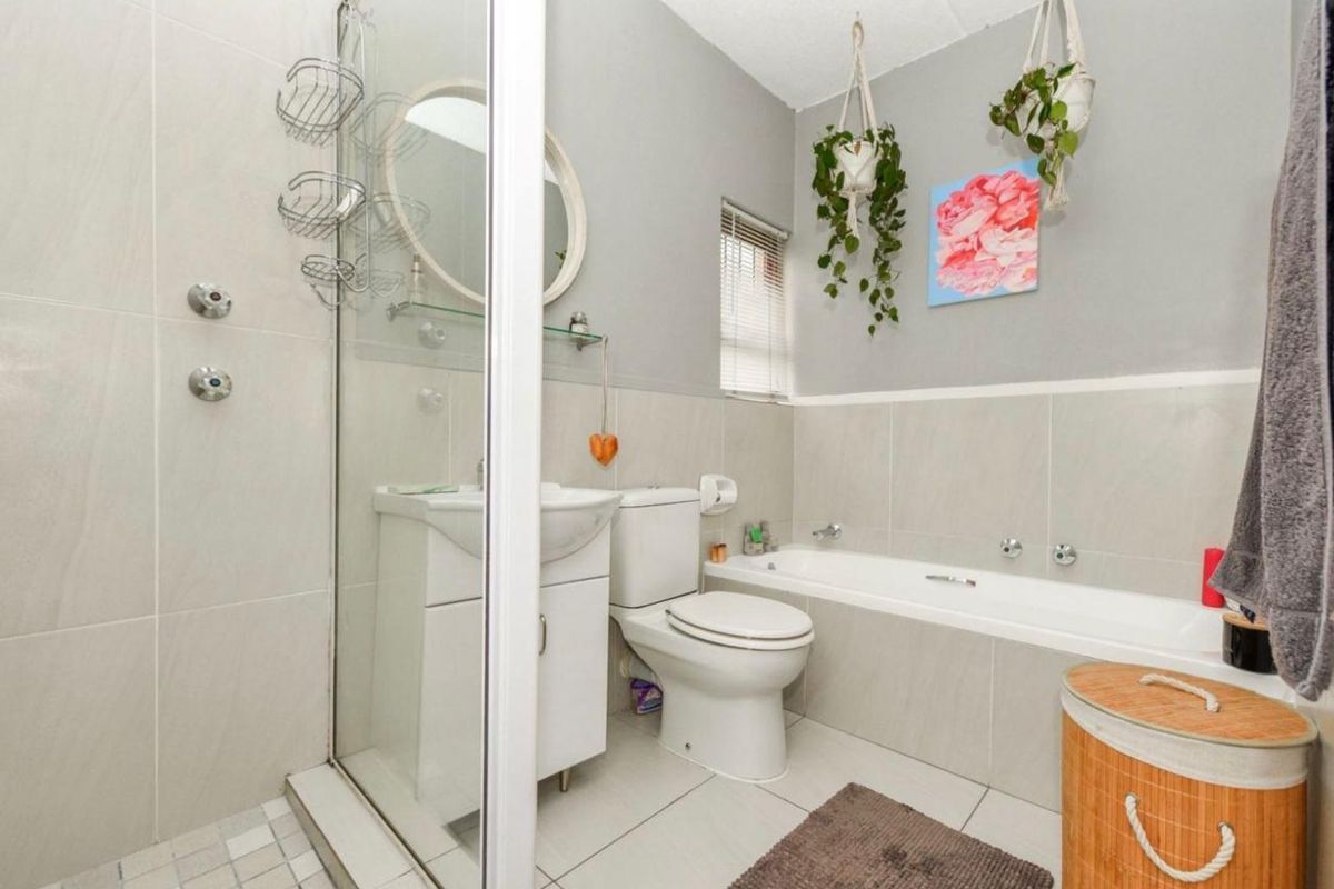 A well-maintained bathroom featuring a glass-enclosed shower, a bathtub, a vanity basin, and a toilet with neutral wall and floor tiling.