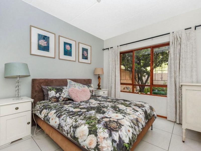 A well-lit bedroom featuring tiled flooring and a large timber-framed window with security bars, offering a view of the garden.