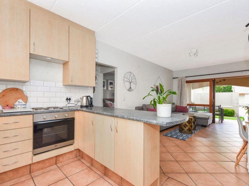 Open-plan kitchen and living area featuring light wood cabinetry, granite-look countertops, subway tile backsplash, and terracotta flooring with direct access to a patio.