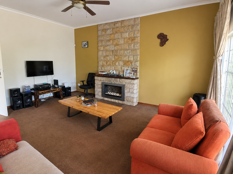 Spacious living room featuring a prominent stone-clad fireplace and ceiling fan, offering a warm and comfortable atmosphere.