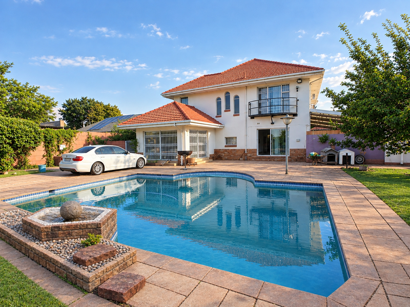 Rear exterior view featuring a swimming pool, stone water feature, tiled patio area, and a two-story house with a balcony.