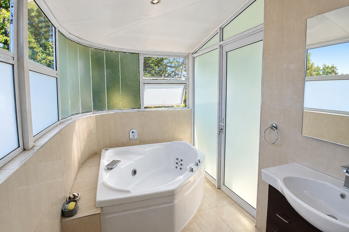 Modern bathroom featuring a corner spa bath, tiled finishes, vanity with basin, and large frosted glass windows providing natural light.