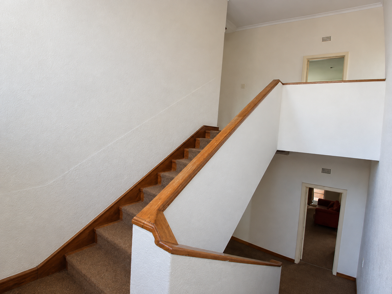 A spacious interior hallway featuring a carpeted staircase with a wooden handrail, connecting multiple levels of the home.