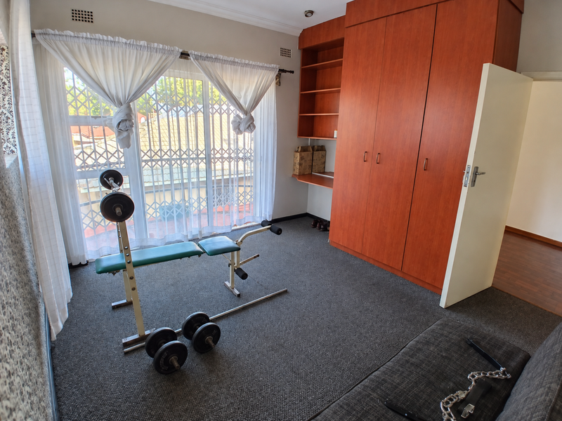 Bedroom featuring built-in wooden cupboards with integrated shelving, carpeted flooring, and a large window with security gate access.