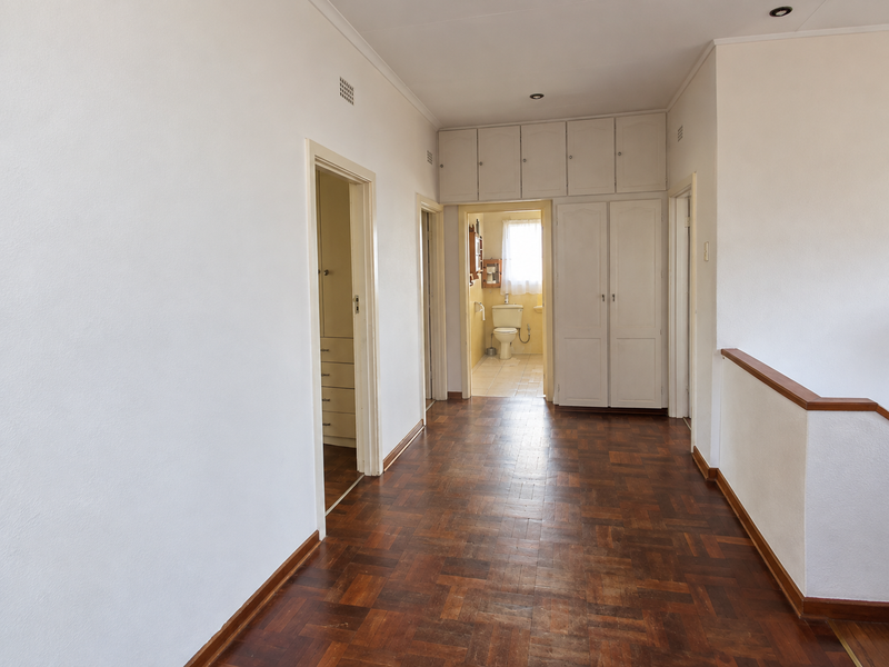 Spacious hallway featuring classic parquet flooring, extensive built-in storage cupboards, and a view through to an adjacent bathroom.