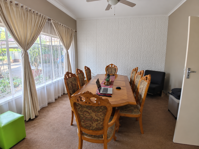 A dining room featuring a textured feature wall, ceiling fan, and large window providing natural light.