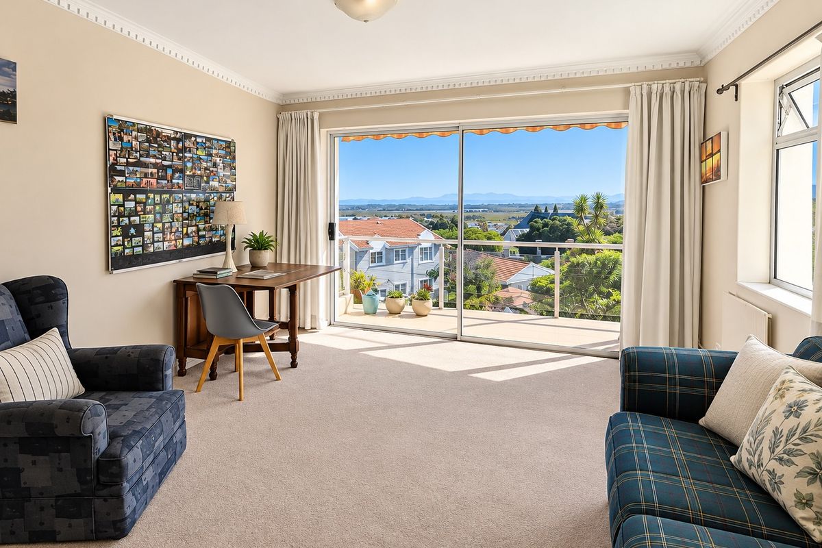 A bright living room featuring crown molding, carpet flooring, and a large sliding glass door that opens onto a balcony with scenic views.