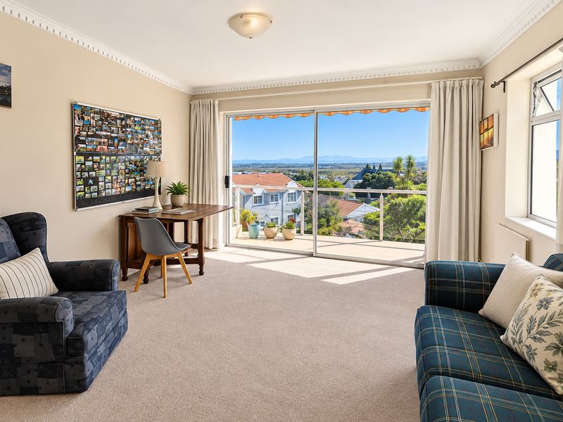 A bright living room featuring crown molding, carpet flooring, and a large sliding glass door that opens onto a balcony with scenic views.
