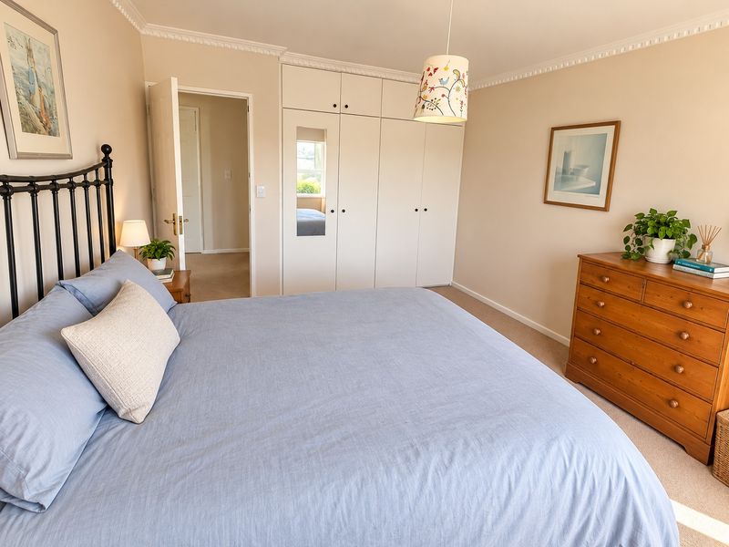 A well-maintained bedroom featuring neutral walls, crown molding, carpeted flooring, and a large built-in wardrobe with integrated mirror.