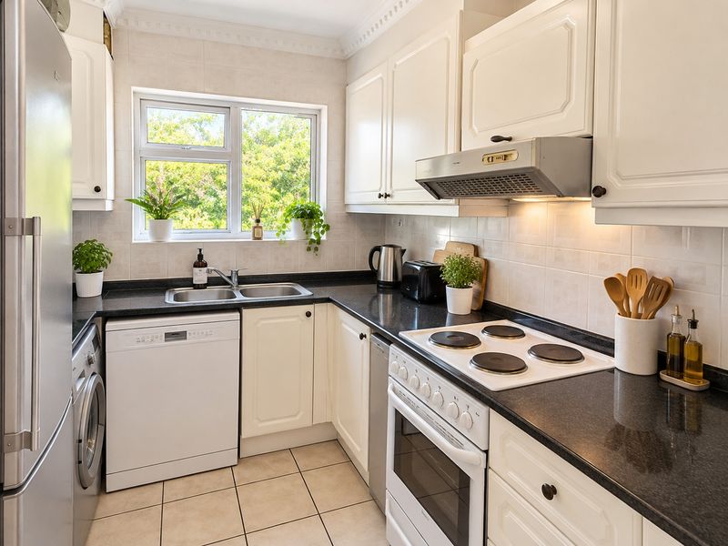 A functional kitchen featuring white cabinetry, dark countertops, a built-in oven with electric hob, and a window providing natural light.