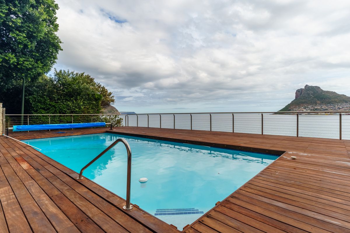 An outdoor swimming pool area featuring timber decking and a stainless steel balustrade, offering expansive coastal and mountain views.