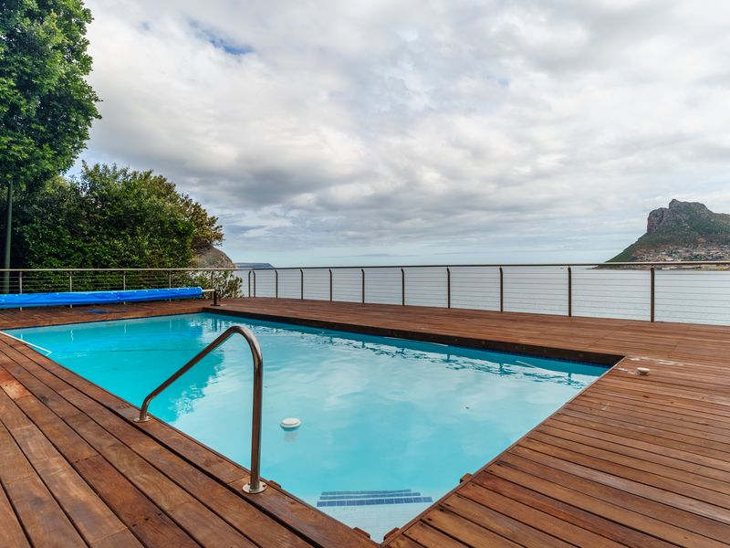 An outdoor swimming pool area featuring timber decking and a stainless steel balustrade, offering expansive coastal and mountain views.