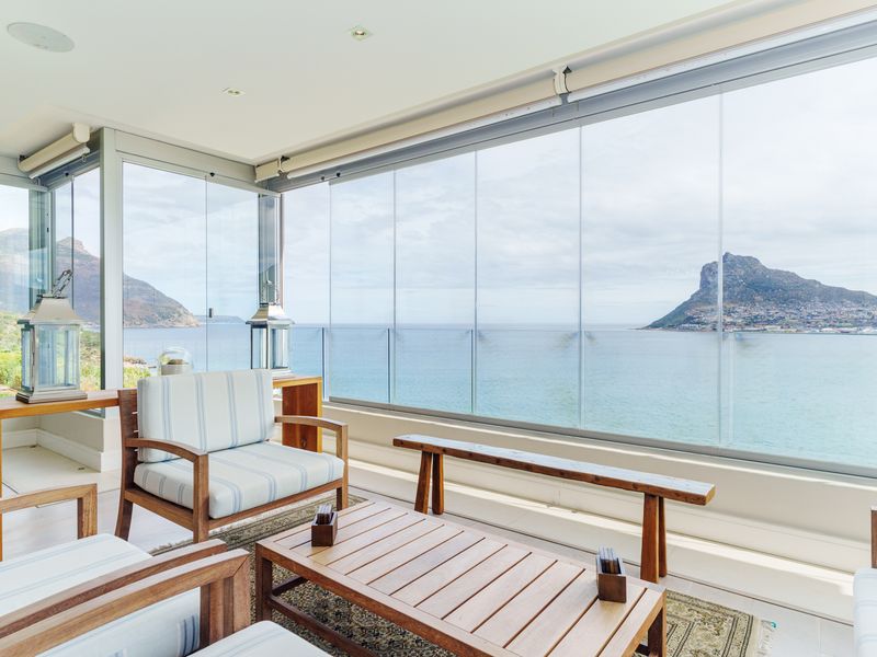 A bright, enclosed balcony featuring frameless glass panels, recessed lighting, and a glass balustrade, offering expansive ocean and mountain views.