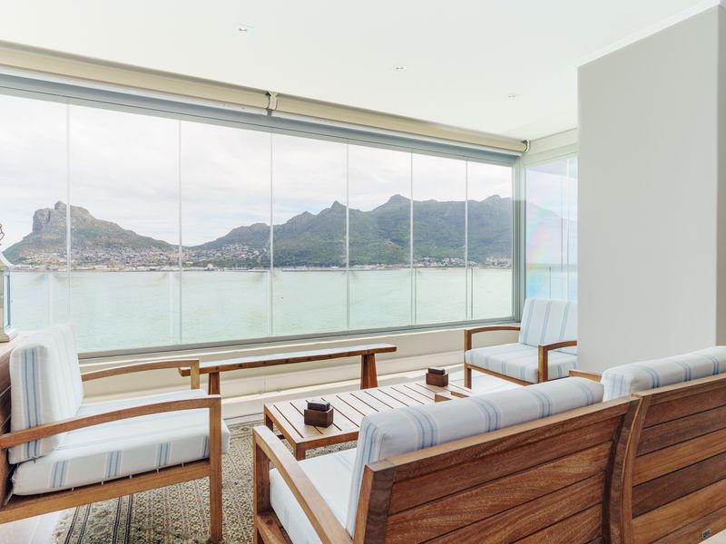 A bright, enclosed balcony featuring frameless glass panels that offer expansive mountain and water views, creating a seamless indoor-outdoor living space.