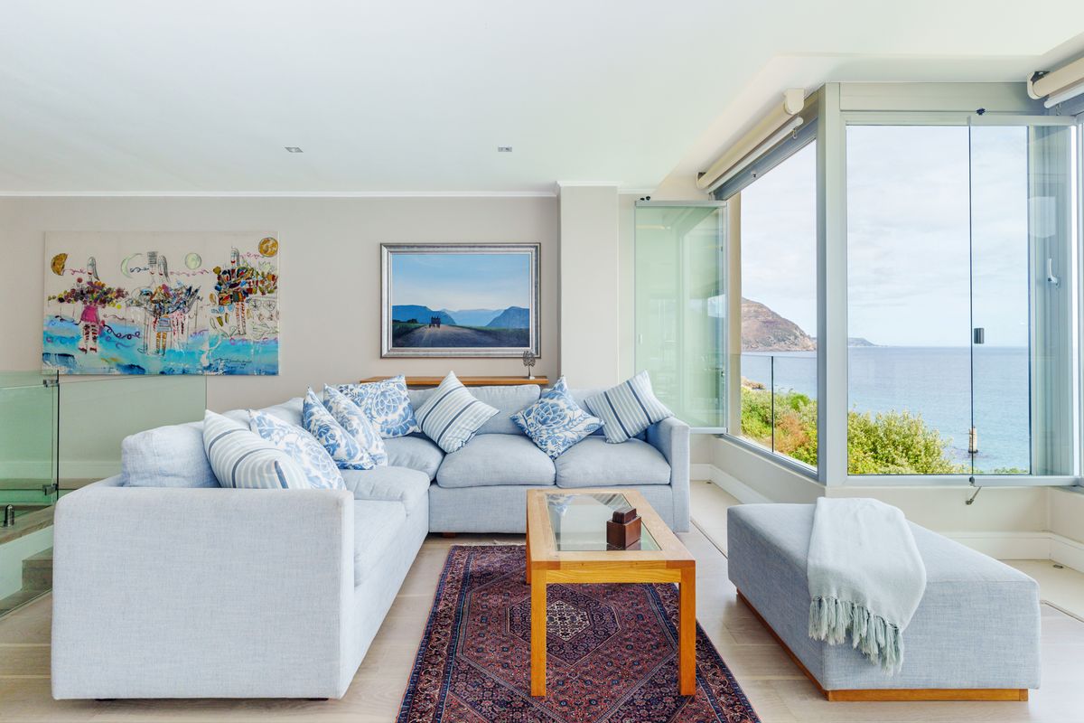 A bright and modern living room featuring large glass doors that open to a scenic coastal view, complemented by neutral finishes and recessed lighting.