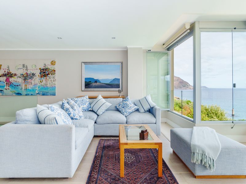 A bright and modern living room featuring large glass doors that open to a scenic coastal view, complemented by neutral finishes and recessed lighting.