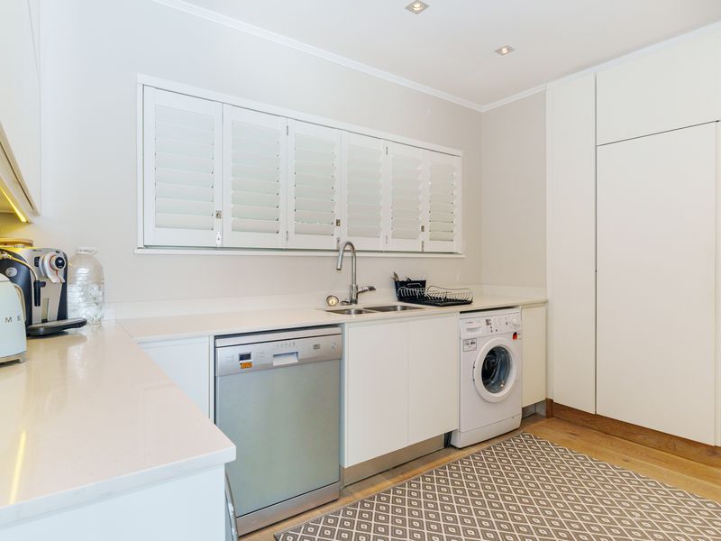 A modern, well-appointed laundry area featuring sleek white cabinetry, quartz countertops, integrated appliances, and plantation shutters for a clean, functional finish.