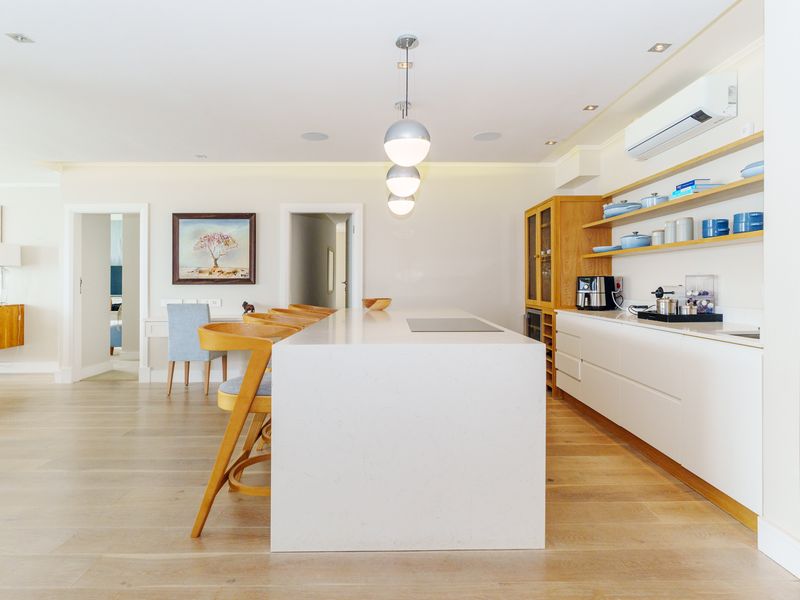 Modern open-plan kitchen featuring a large stone island, sleek cabinetry, open shelving, and high-quality hardwood flooring in a bright, well-maintained living space.