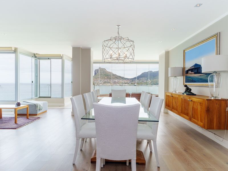 Spacious open-plan living and dining area featuring light wood flooring, recessed lighting, and expansive glass doors offering panoramic coastal and mountain views.