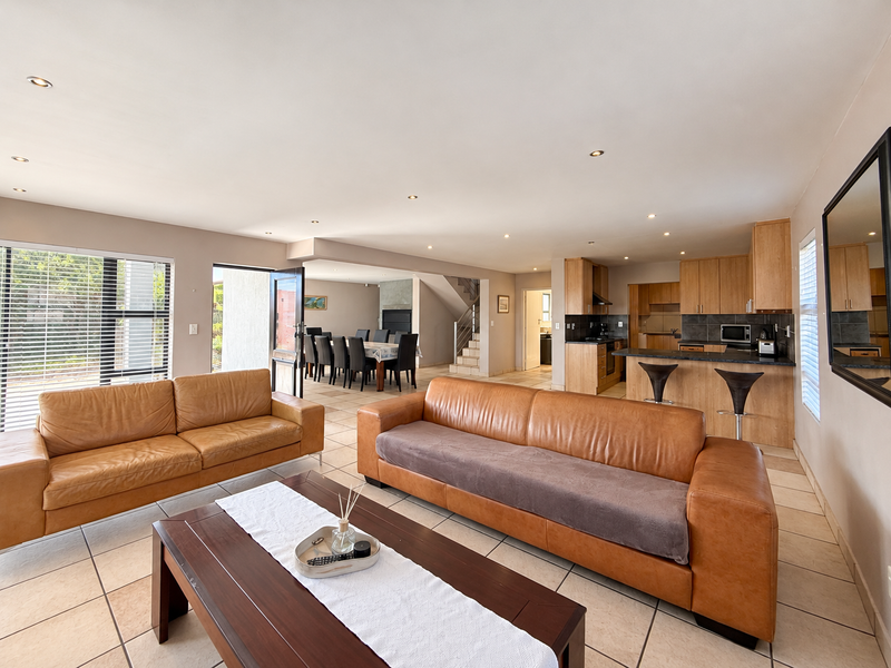 Spacious open-plan living area featuring a kitchen with breakfast bar, tiled flooring, recessed lighting, and seamless flow to the dining space and outdoor access.