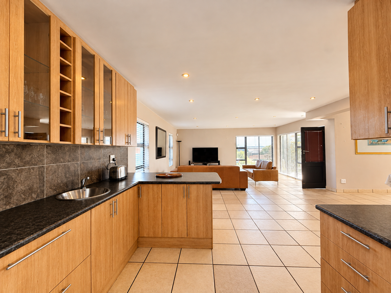 Spacious open-plan kitchen and living area featuring light wood cabinetry, dark countertops, tiled flooring, and abundant natural light through large windows.