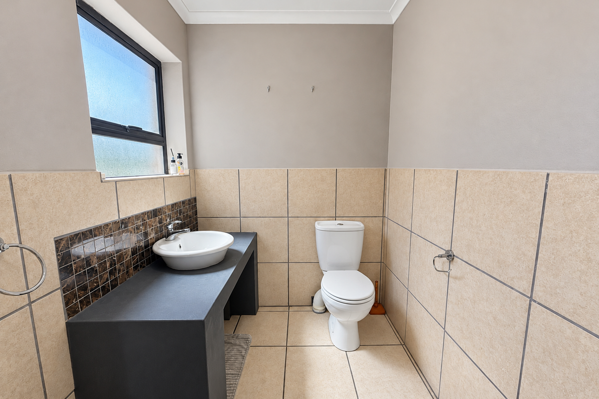 A clean, functional bathroom featuring a vessel sink on a dark vanity countertop, a standard toilet, and neutral wall and floor tiling.