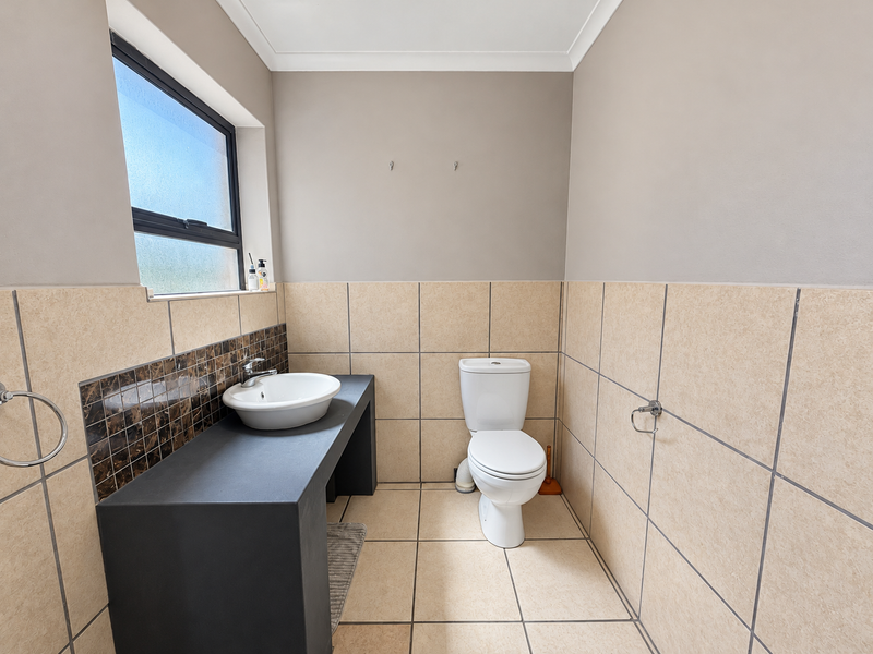 A clean, functional bathroom featuring a vessel sink on a dark vanity countertop, a standard toilet, and neutral wall and floor tiling.